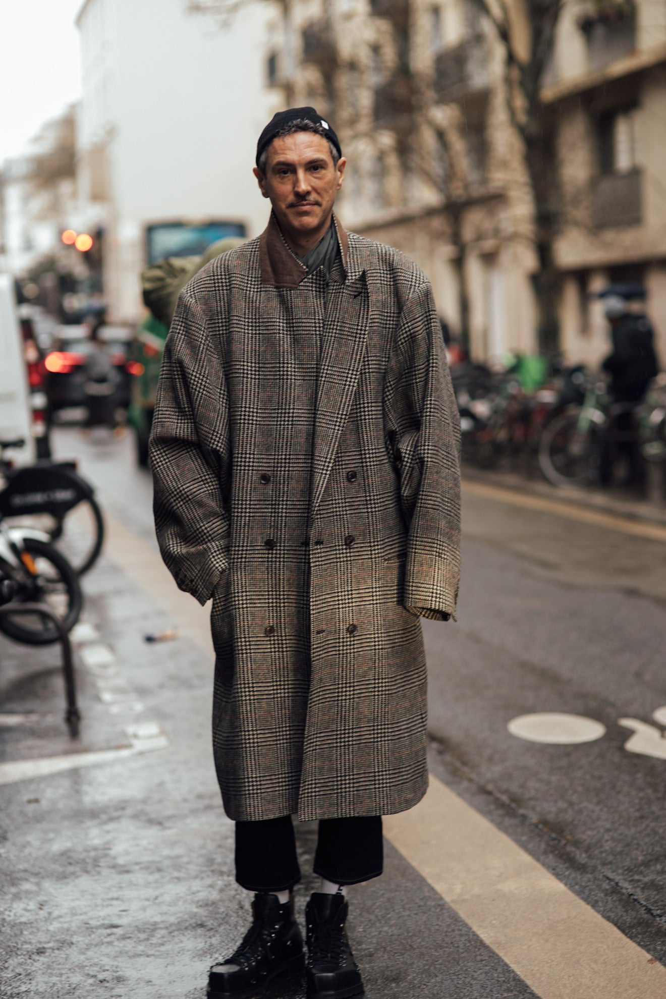 A man wearing an oversized double-breasted trench coat that features a fine check print and oversized lapels